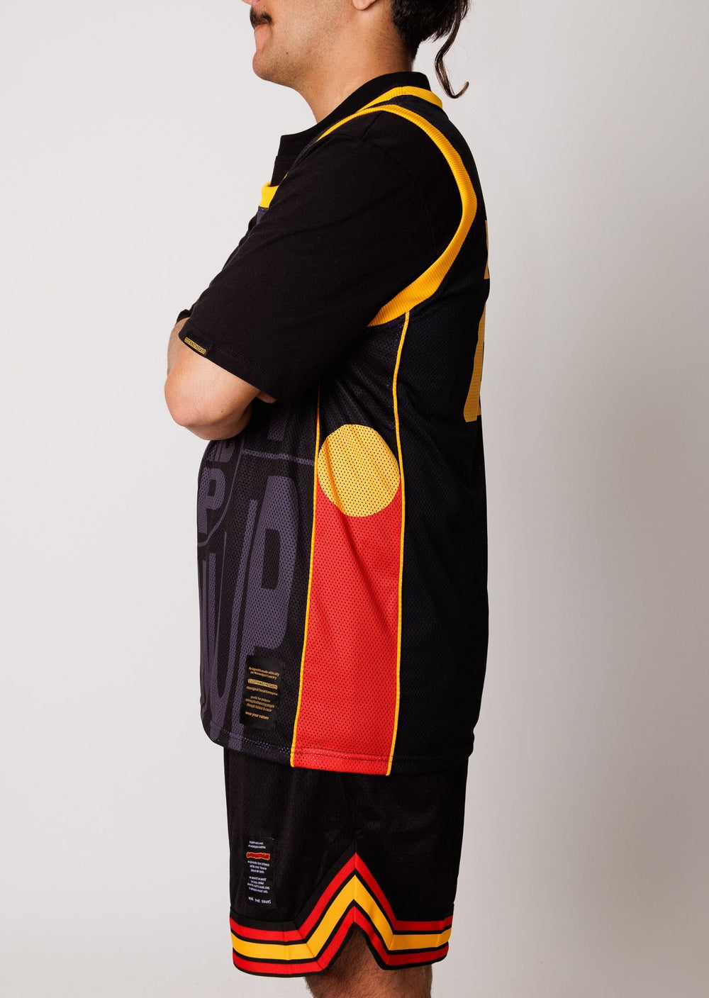 Clothing The Gaps. Get Up! Stand Up! Show Up! Basketball Jersey. Featuring a sublimated design with a black background and 'Get Up! Stand Up! Show Up!' on a contrasting dark grey on front of singlet. Aboriginal flags done the side panel. Yellow piping and knitted bands around arms and neck. Bold yellow pocket sized 22 on left corner of front. On Back of jersey is 22 in yellow big in centre.