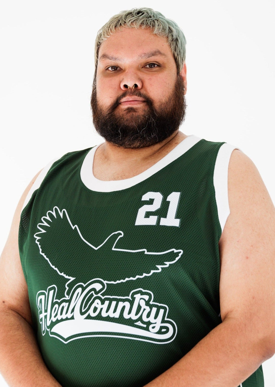 Clothing The Gaps. Heal Country Basketball Jersey. Dark green back ground with outlined Bunjil the Eagle, the creator spirit and 'Heal Country' text in white on centre of jersey. '21' in bold white numbers on left corner of front. On back of jersey '21' in big white letters in centre. Giving us Boston Celtics energy with white knitted bands around arms and neck.