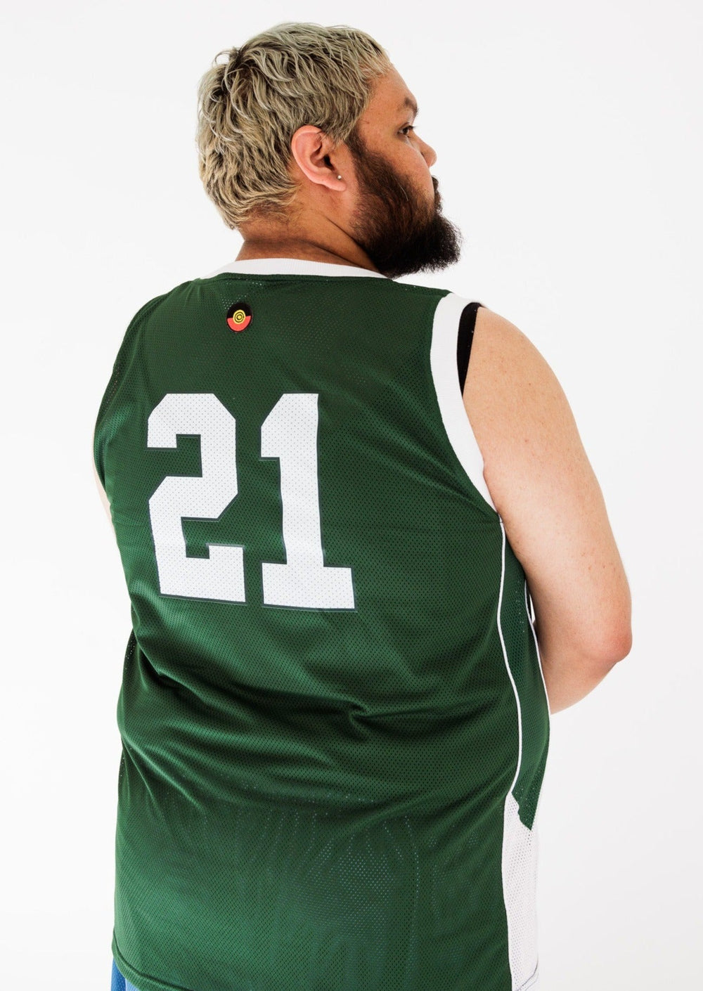 Clothing The Gaps. Heal Country Basketball Jersey. Dark green back ground with outlined Bunjil the Eagle, the creator spirit and 'Heal Country' text in white on centre of jersey. '21' in bold white numbers on left corner of front. On back of jersey '21' in big white letters in centre. Giving us Boston Celtics energy with white knitted bands around arms and neck.