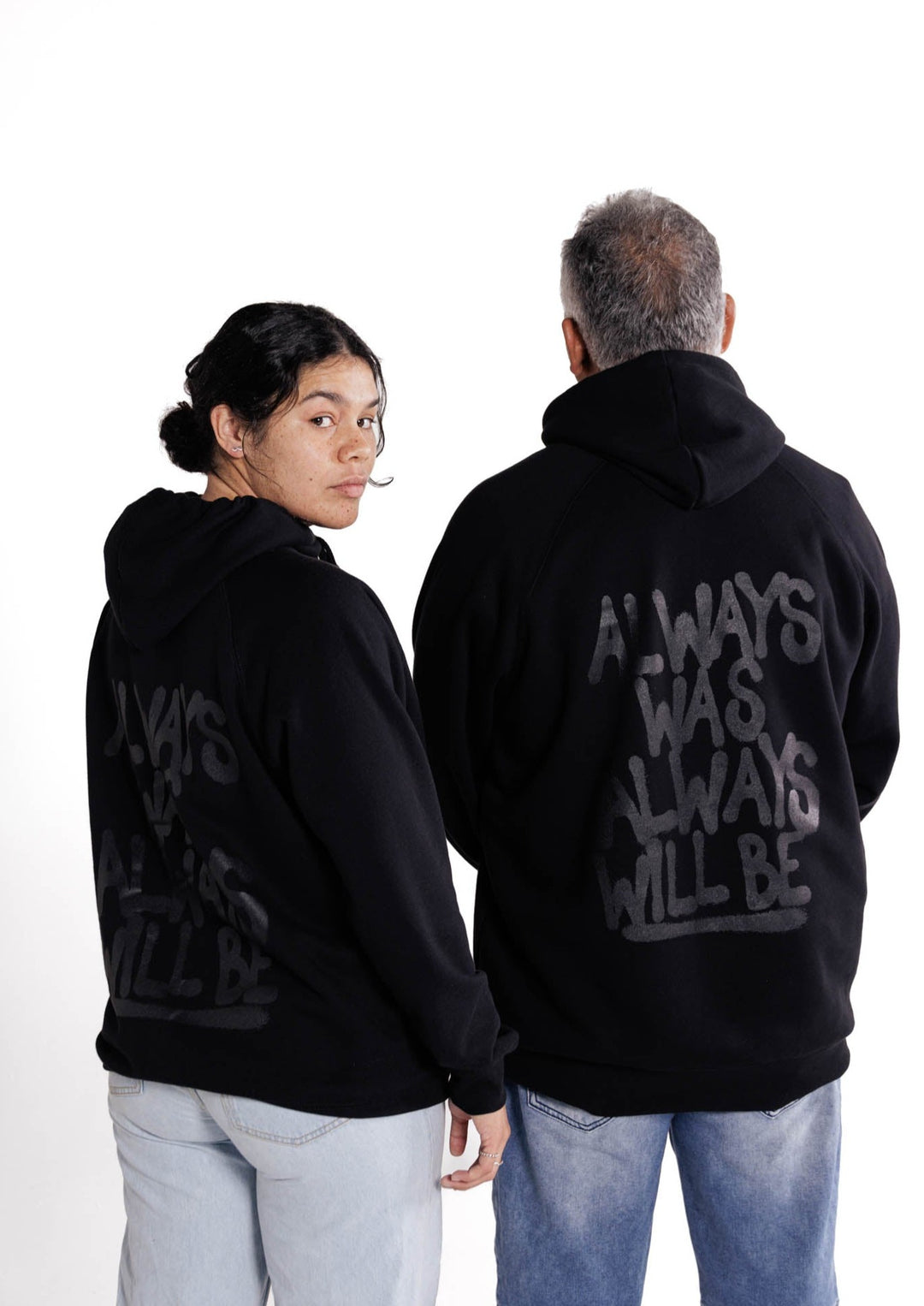 Clothing The Gaps. Black hoodie with Aboriginal flag outline embroidered in black on the front. On the back of the hoodie a powerful Aboriginal chant 'Always Was, Always Will Be' looks like it has been sprayed on with a black spray can! The Clothing the Gaps circle logo patch provides a sneaky little pop of red, black and yellow on the sleeve.