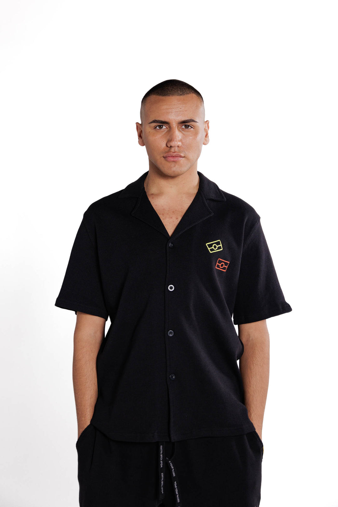 Clothing The Gaps. Waffle Shirt.  Black button up shirt in cotton waffle material with red and yellow Aboriginal flag outlines on left pocket area of shirt. V neck style shirt with basic shirt collar.