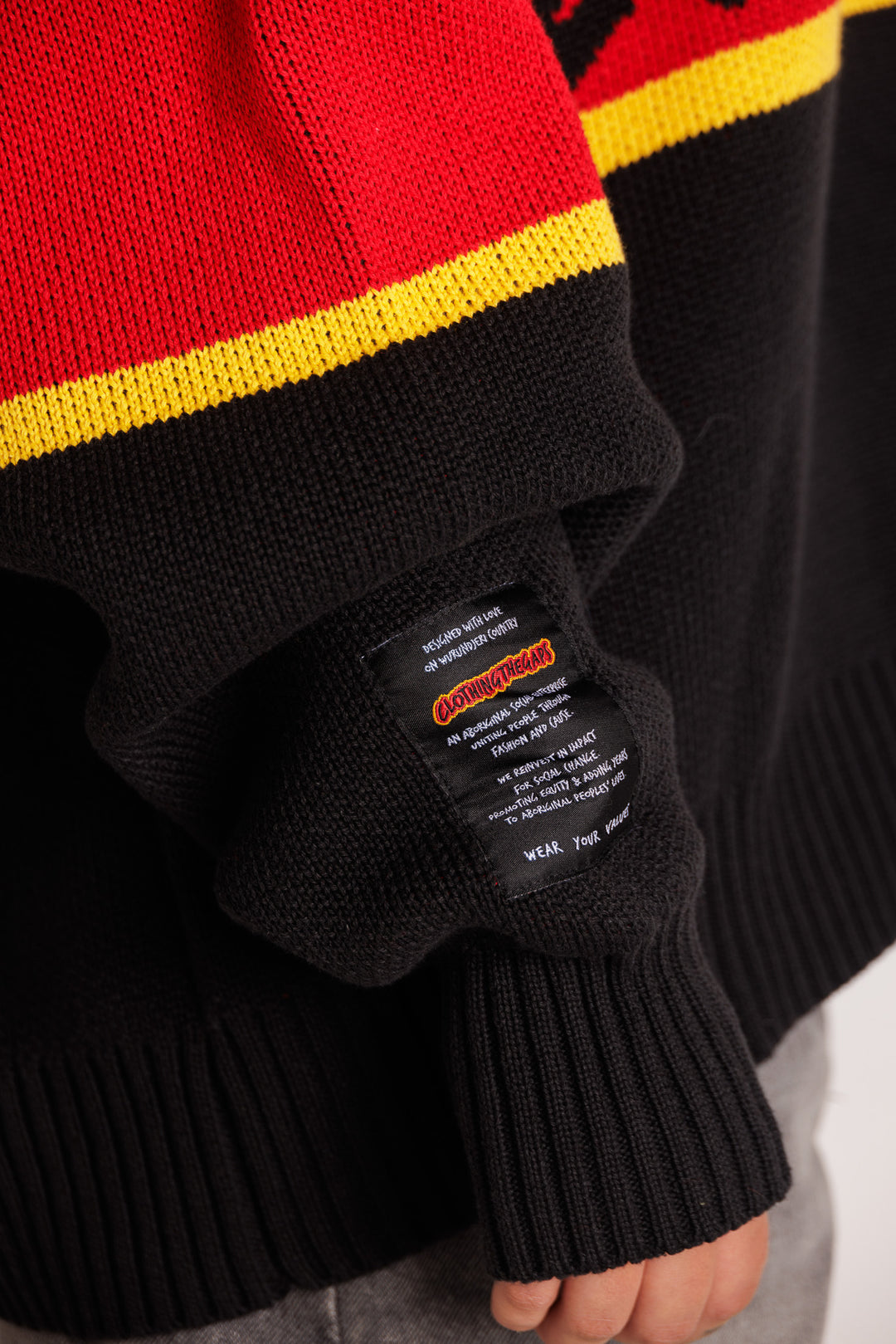 Clothing The Gaps. Power Knit Jumper. Red, black and yellow colorway heavyweight 100% cotton oversized boxy fit. Black base with thick yellow top and bottom lines and red fill in mid section of jumper that flows into same pattern on sleeves. In red section on front of jumper in bold hand-written type capital text reads 'Always was' and on back in same text 'Always will be.' With black knitted cuffs and waistband.