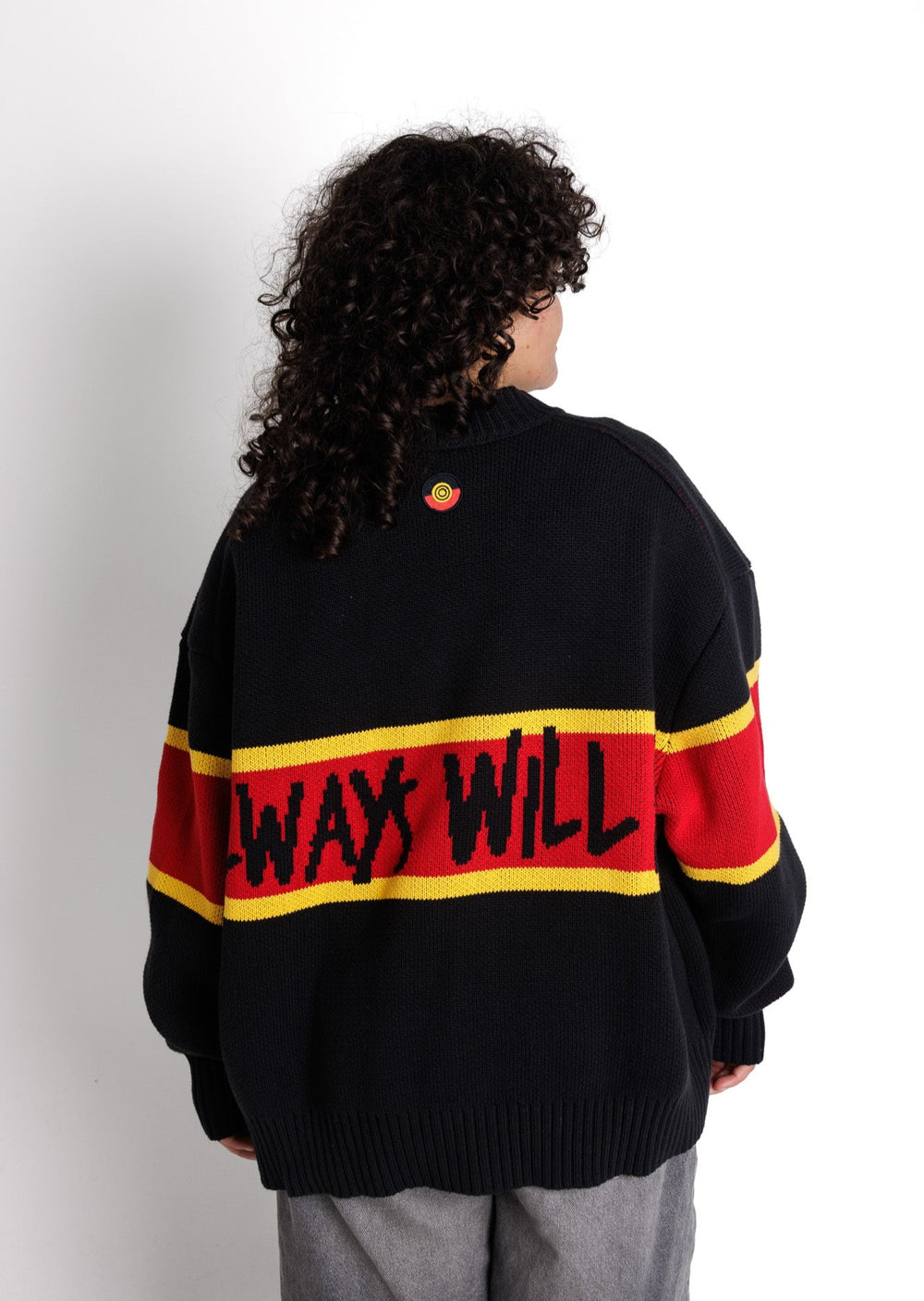 Clothing The Gaps. Power Knit Jumper. Red, black and yellow colorway heavyweight 100% cotton oversized boxy fit. Black base with thick yellow top and bottom lines and red fill in mid section of jumper that flows into same pattern on sleeves. In red section on front of jumper in bold hand-written type capital text reads 'Always was' and on back in same text 'Always will be.' With black knitted cuffs and waistband.