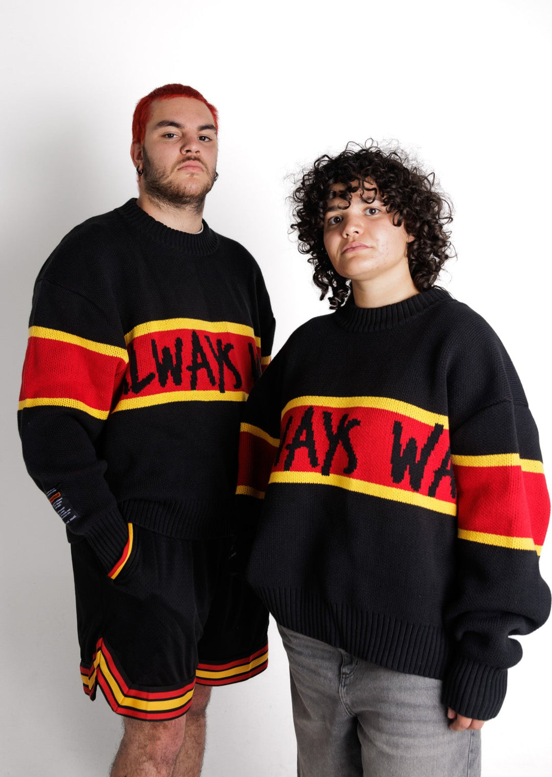 Clothing The Gaps. Power Knit Jumper. Red, black and yellow colorway heavyweight 100% cotton oversized boxy fit. Black base with thick yellow top and bottom lines and red fill in mid section of jumper that flows into same pattern on sleeves. In red section on front of jumper in bold hand-written type capital text reads 'Always was' and on back in same text 'Always will be.' With black knitted cuffs and waistband.