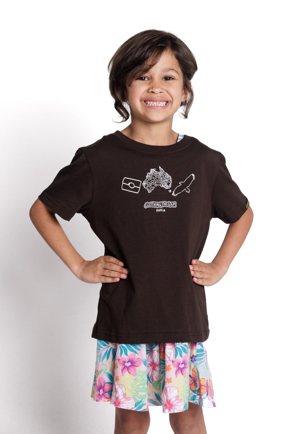 Clothing The Gaps. Kids Icon Tee. Expresso dark brown tee featuring Aboriginal symbols of resistance and culture including a white outline of the Aboriginal flag, a white outlined decolonised map of “Australia” and a white outlined Bunjil, a well known wedge-tailed eagle - who is the spiritual creator and protector of the Kulin Nation in Victoria. These symbols are on the front of the tee across the chest.
