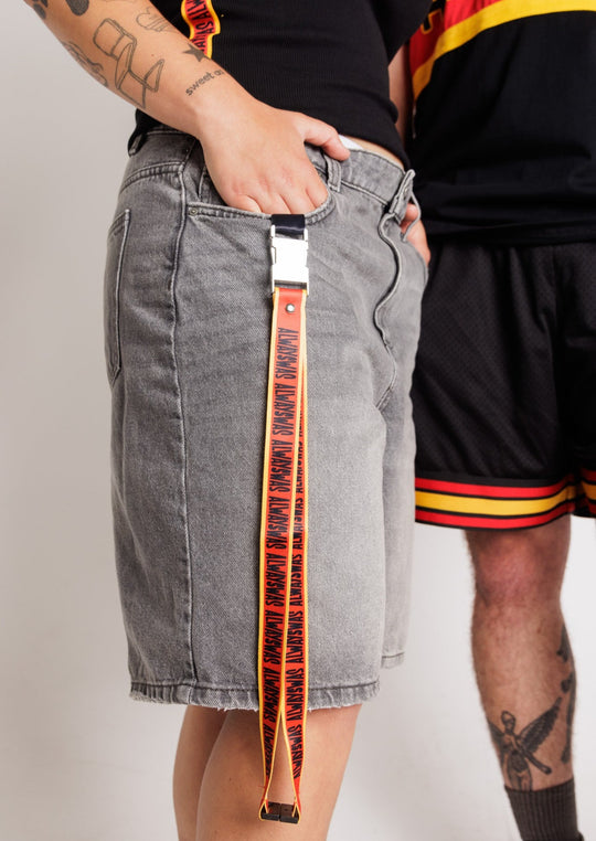 Clothing The Gaps. Power Lanyard. Thick strap with black 'always was' text on a red background with a yellow trim repeated. With an extra large silver metal clasp and engraved with the Clothing The Gaps logo. Black safety clip at back of neck. Silver metal clip at end of lanyard to attach what you would like.