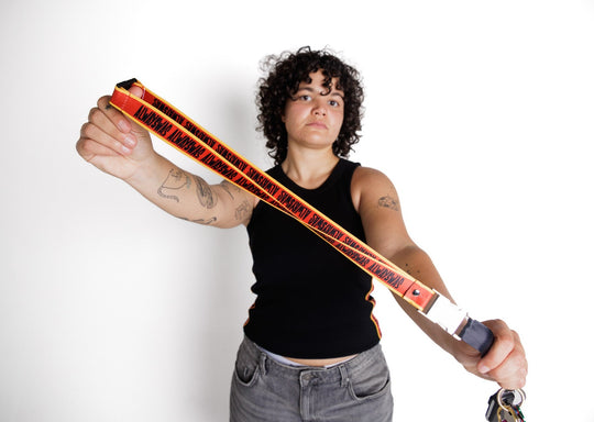 Clothing The Gaps. Power Lanyard. Thick strap with black 'always was' text on a red background with a yellow trim repeated. With an extra large silver metal clasp and engraved with the Clothing The Gaps logo. Black safety clip at back of neck. Silver metal clip at end of lanyard to attach what you would like.