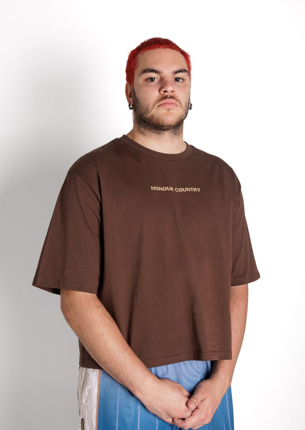 Clothing The Gaps. Honour Country Crop Tee. Chocolate brown cropped tee. On front in contrasting light brown 'Honour Country' small in centre across chest in bold capital text. On back in same text big back piece 'Honour and respect Aboriginal and Torres Strait Islander people as the rightful custodians of country.' 