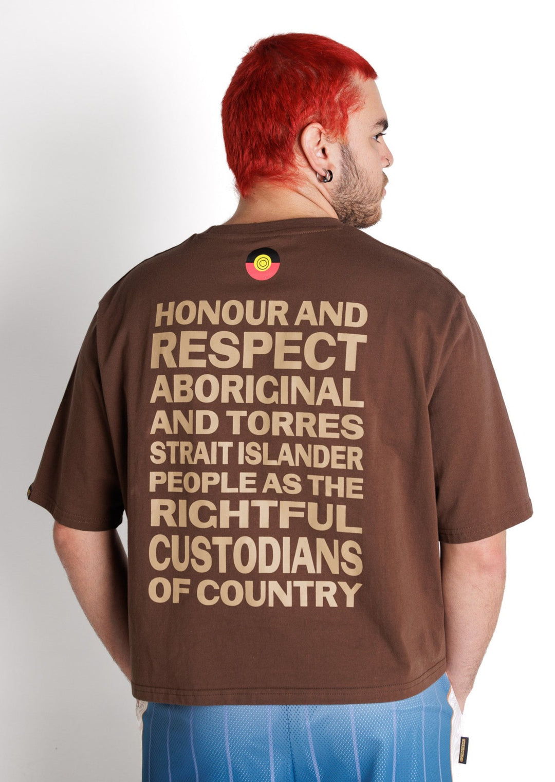 Clothing The Gaps. Honour Country Crop Tee. Chocolate brown cropped tee. On front in contrasting light brown 'Honour Country' small in centre across chest in bold capital text. On back in same text big back piece 'Honour and respect Aboriginal and Torres Strait Islander people as the rightful custodians of country.' 