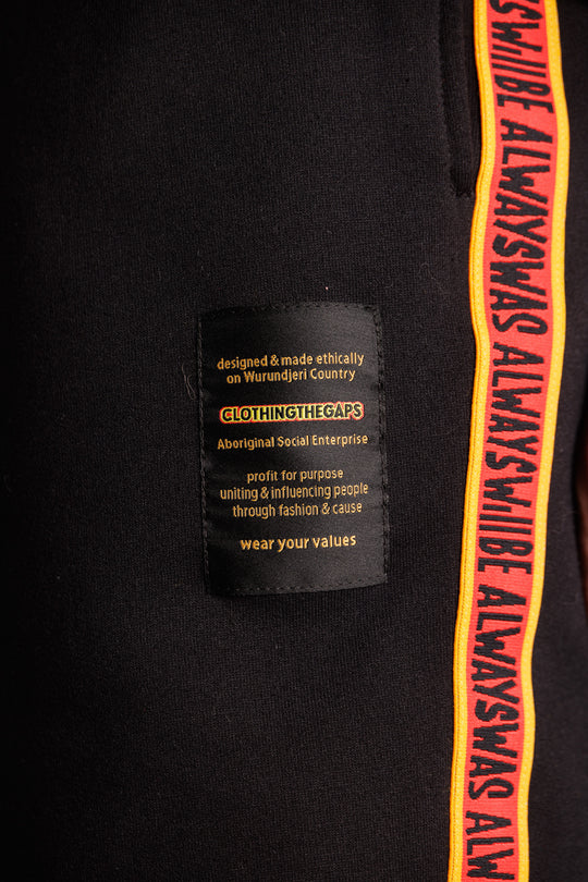 Clothing the Gaps. Black cotton Pants. With black drawstrings. Elastic cuts and waistband. Embroiled Clothing The Gaps logo. Black 'always was always will be' text on a red background with a yellow trim. In a cotton tape strip going down both sides of pants.