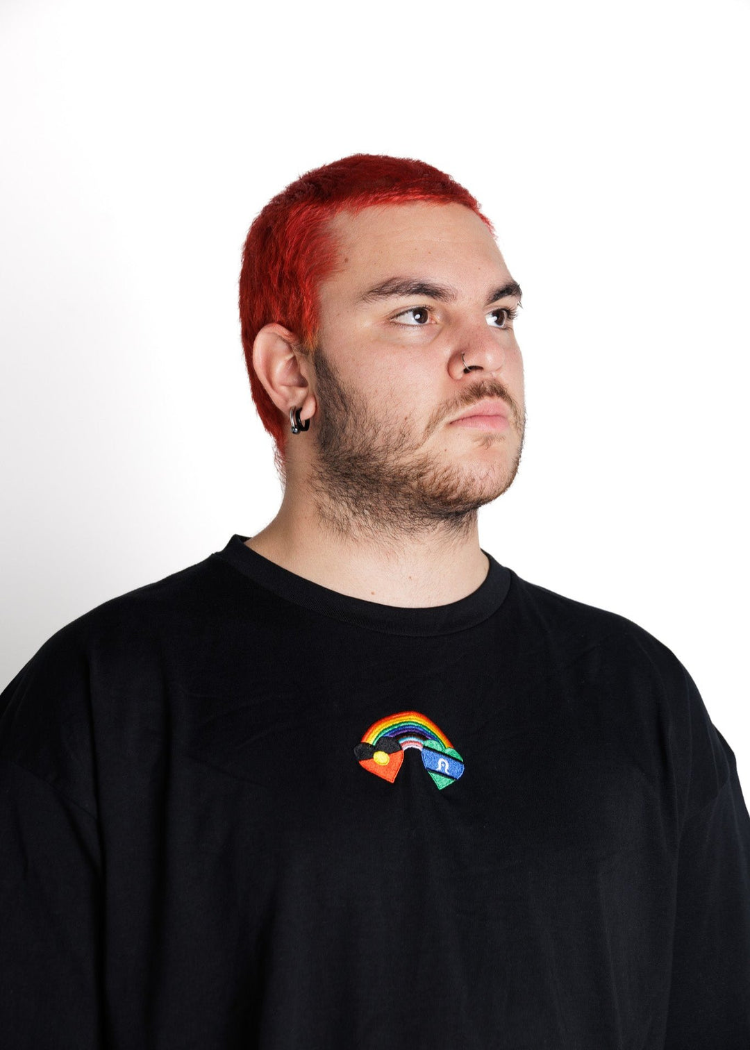 Clothing The Gaps. Blak Rainbow Luv Crop. All black boxy crop tee with  a heart featuring the Aboriginal flag at the start of a rainbow and at the end of the rainbow the Torres Strait Islander flag. This design is embroidered on the front of the t-shirt. The rainbow includes the colours from the progress pride flag. Show your pride or support for First Nations LGBTQIAS&B+ Community.