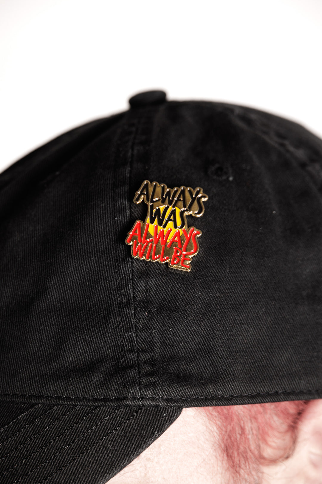 Clothing The Gaps. Pin with Black, yellow and red 'always was always will be' text outlined in gold with a gold backing.
