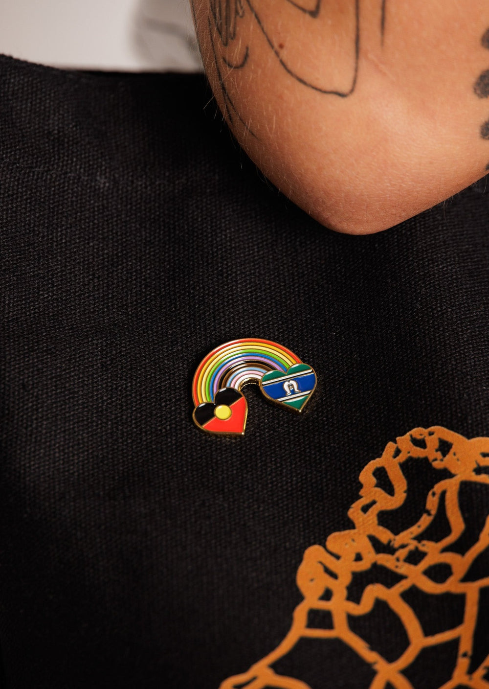 Clothing The Gaps. Rainbow Mob pin. Pin with Aboriginal flag in love heart shape at the start of a rainbow and at the end of the rainbow the Torres Strait Islander flag in love heart shape. The rainbow includes the colours from the progress pride flag. Show your pride or support for First Nations LGBTQIAS&B+ Community.