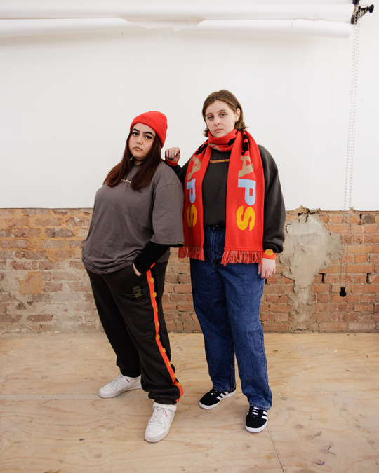 Clothing The Gaps. Charcoal Flag Track Pants. Charcoal dark grey track pants with Aboriginal flag tape down the sides. Has a elastic waist with charcoal grey draw strings and cuffed ankles.