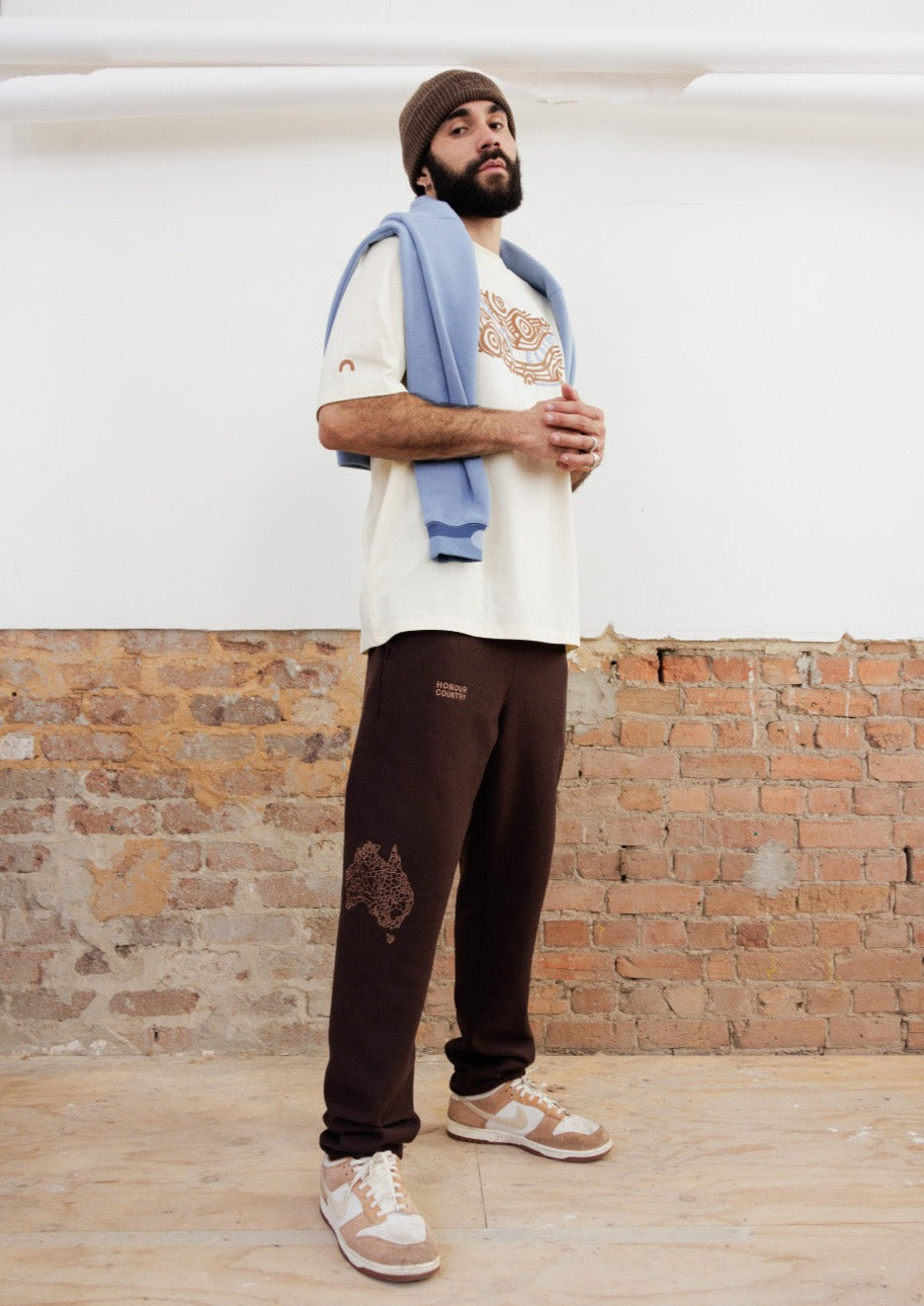 Clothing The Gaps. Brown honour country track pants. Chocolate brown warm track pants. With embroidered decolonised map of 'Australia' in tonal lighter brown on side of right knee and above the embroidered phrase 'Honour Country' in the same tonal lighter brown on middle of right thigh. Features deep side pockets, elastic waist with brown draw strings.