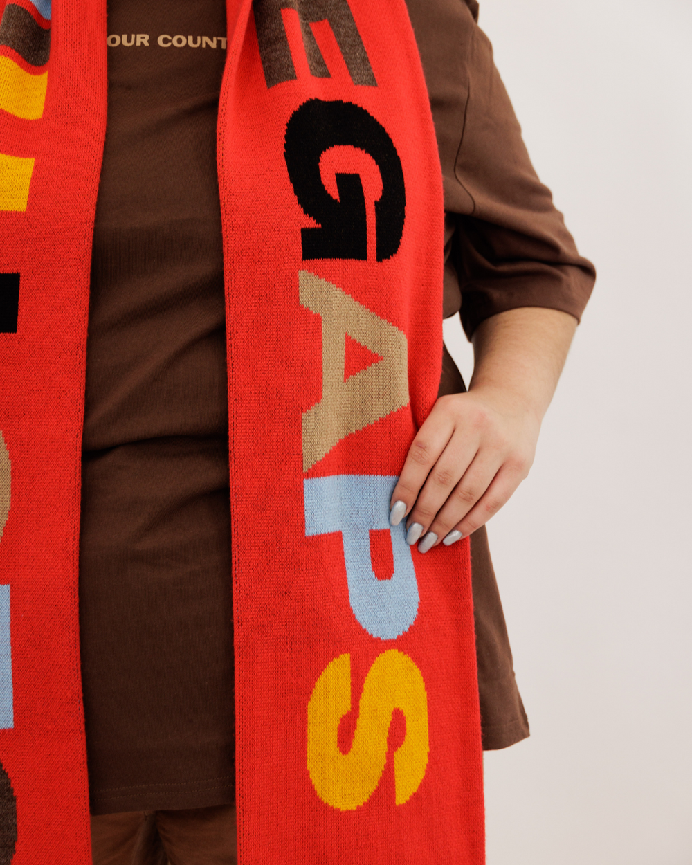 Clothing the gaps. Red CTG Scarf. Long thick red scarf with big letters reading 'Clothing the gaps' with letters in alternating colours of light blue, cream, brown, yellow and black. Red and light blue at ends of scarf.