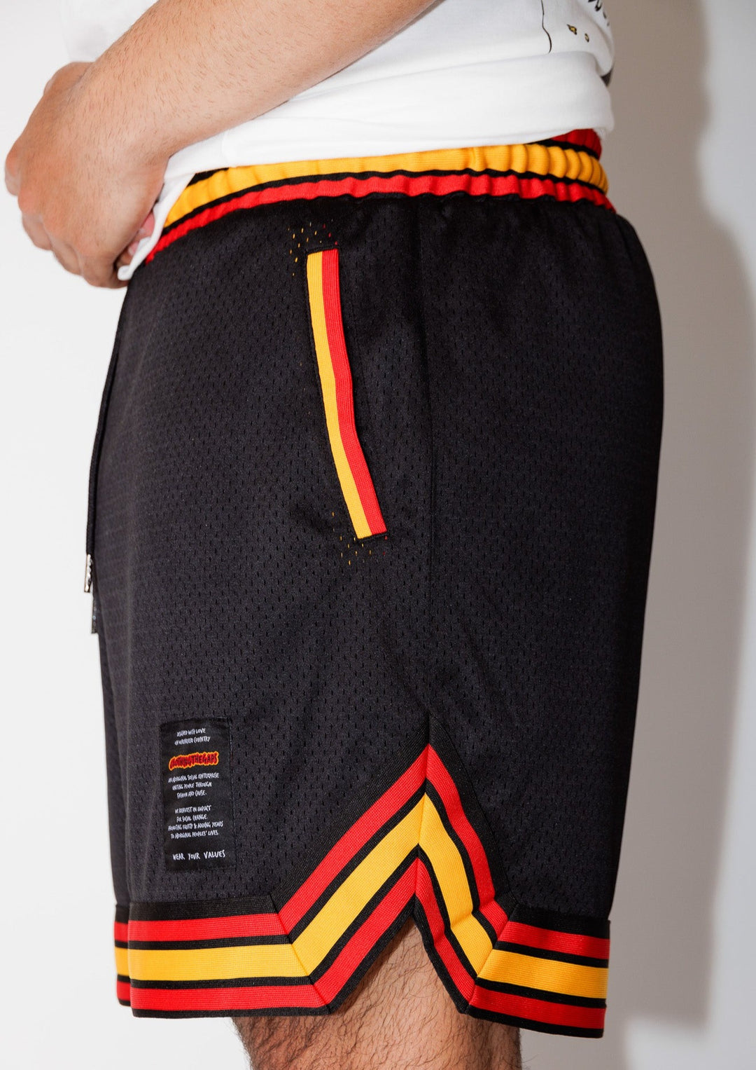 Clothing The Gaps. Blak Basketball Shorts. Retro look with red, black and yellow stripes around bottom of shorts, on pocket opening and around waist band. Rest of the shorts are a black mesh material. Has a elastic waist, black drawstrings, deep pockets and clothing the gaps patch on corner of left leg.