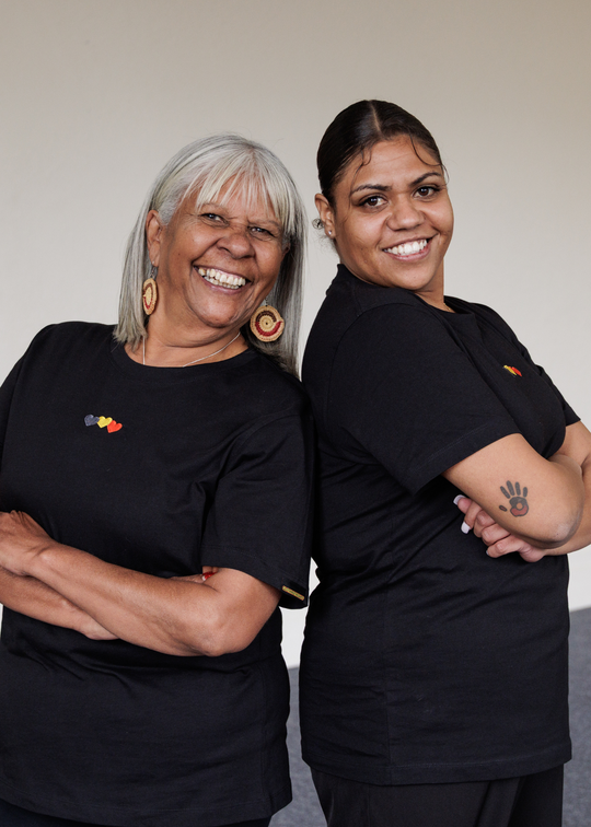 Two women wearing Blak Luv CLothing The Gaps black shirts with visible logos, standing against a plain background.
