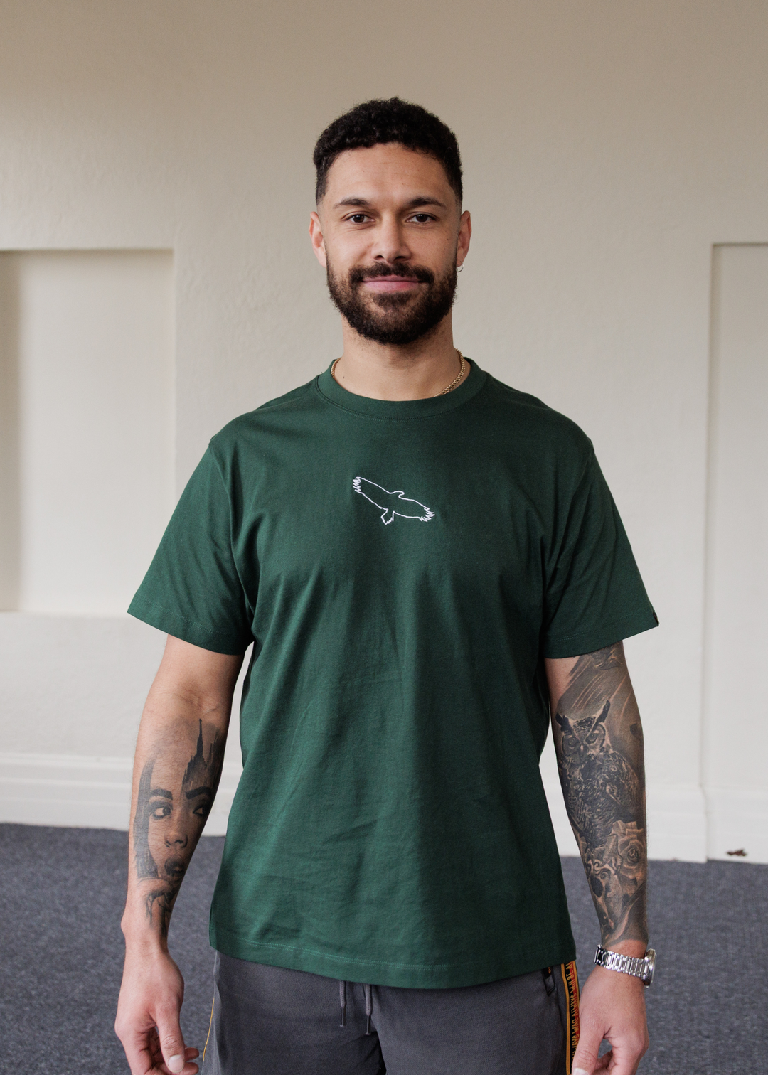 Man wearing a green Bunjil eagle clothing the gaps t-shirt with a logo indoors