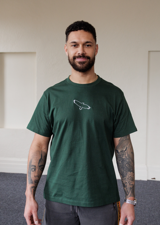 Man wearing a green Bunjil eagle clothing the gaps t-shirt with a logo indoors