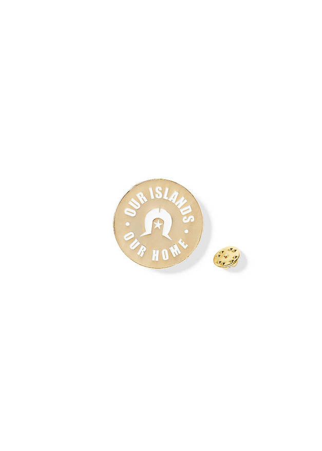 Clothing The Gaps. Our Islands Our Home Pin. Circle gold pin with words 'Our Islands Our Home' in white capital bold text and a white Dhari in the centre.