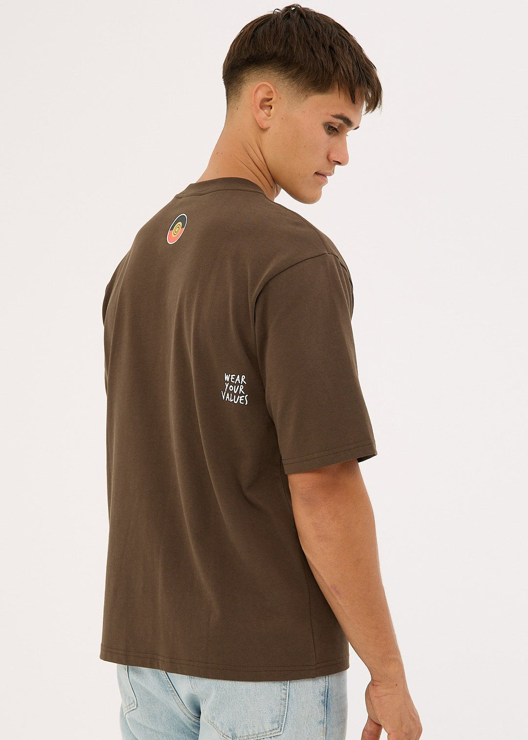 Man wearing a Clothing The Gaps Icon Tee Brown t-shirt with text on the back, standing against a white background