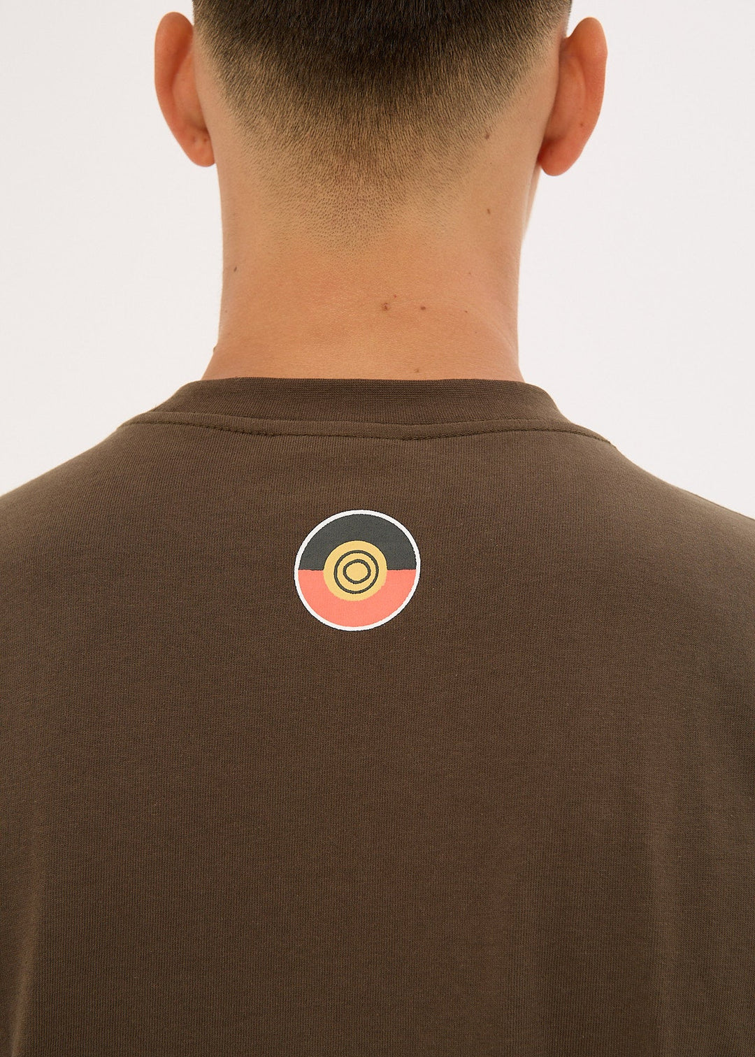 Clothing The Gaps Icon Tee Brown t-shirt with a colorful logo on the back, worn by a person.