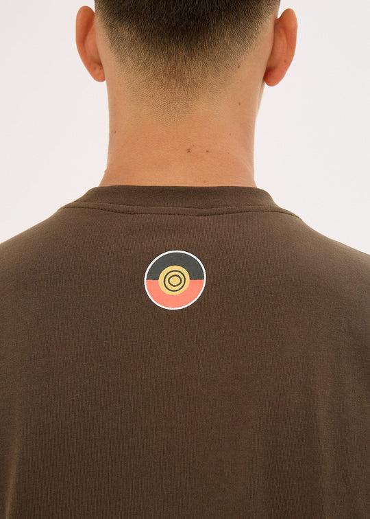 Clothing The Gaps Icon Tee Brown t-shirt with a colorful logo on the back, worn by a person.
