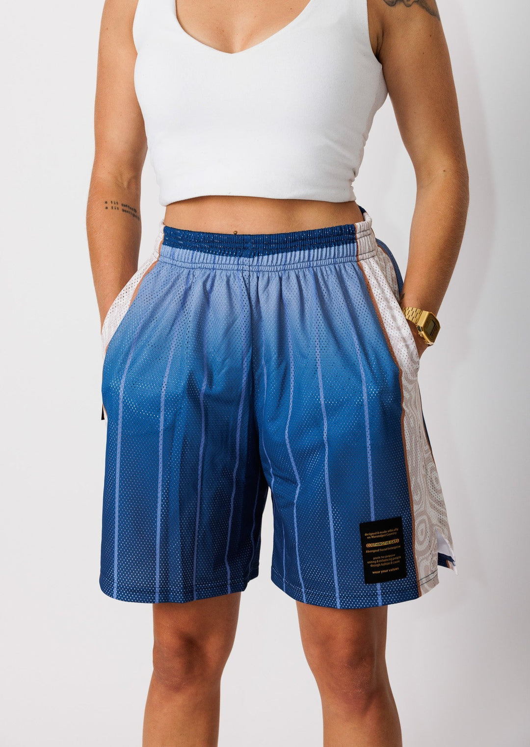 Clothing The Gaps. Naarm Basketball Shorts. Retro look with Mesh retro look crafted with a sublimated blue gradient finish light blue vertical lines going down leg. Cream/tan aboriginal  artwork strip going down side of both legs. Has a elastic waist, deep pockets and clothing the gaps patch on corner of left leg. 