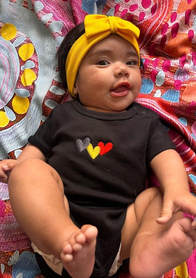 Clothing The Gaps. Blak Luv Bubup Baby Romper. Organic Cotton. All black with  Red, black and yellow hearts embroiled on front. Short sleeve, with clip buttons on left shoulder and on the bottom.