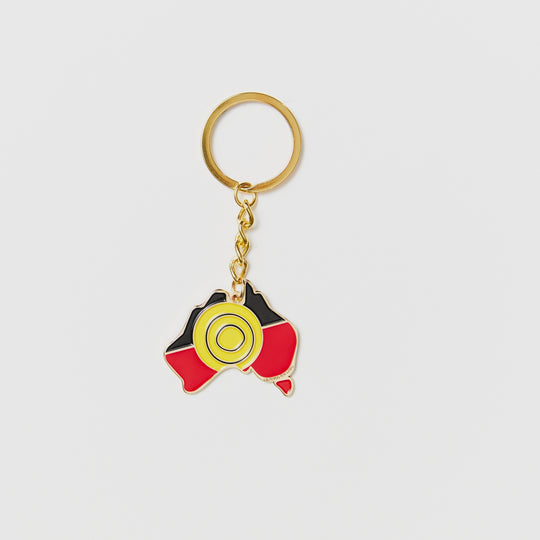 Clothing The Gaps. Keyring with gold chain and loop attached to black, yellow and red aboriginal flag colours shaped inside map of Australia with skinny gold outline.