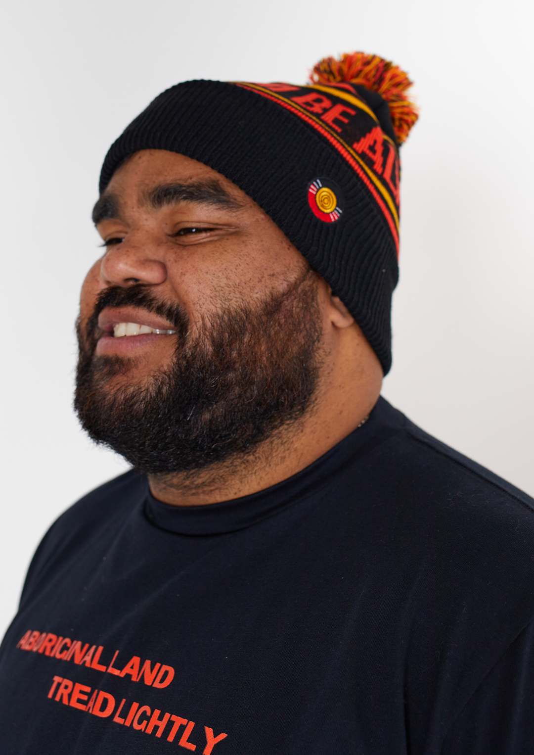 Clothing The Gaps. Power Beanie. Black base with two skinny red and yellow lines above and below bold capital red text 'Always was, Always will be.' Red, black and yellow pom on top of beanie. Embroidered clothing the gap.