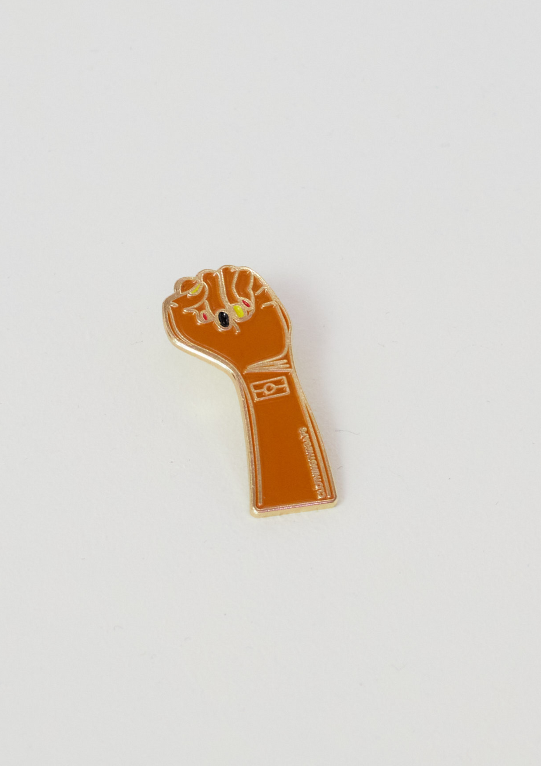 Clothing The gaps. Resistance Pin. Detailed brown resistance fist with red, black and yellow painted nails and aboriginal flag on wrist of fist. With gold outlines and backing. 