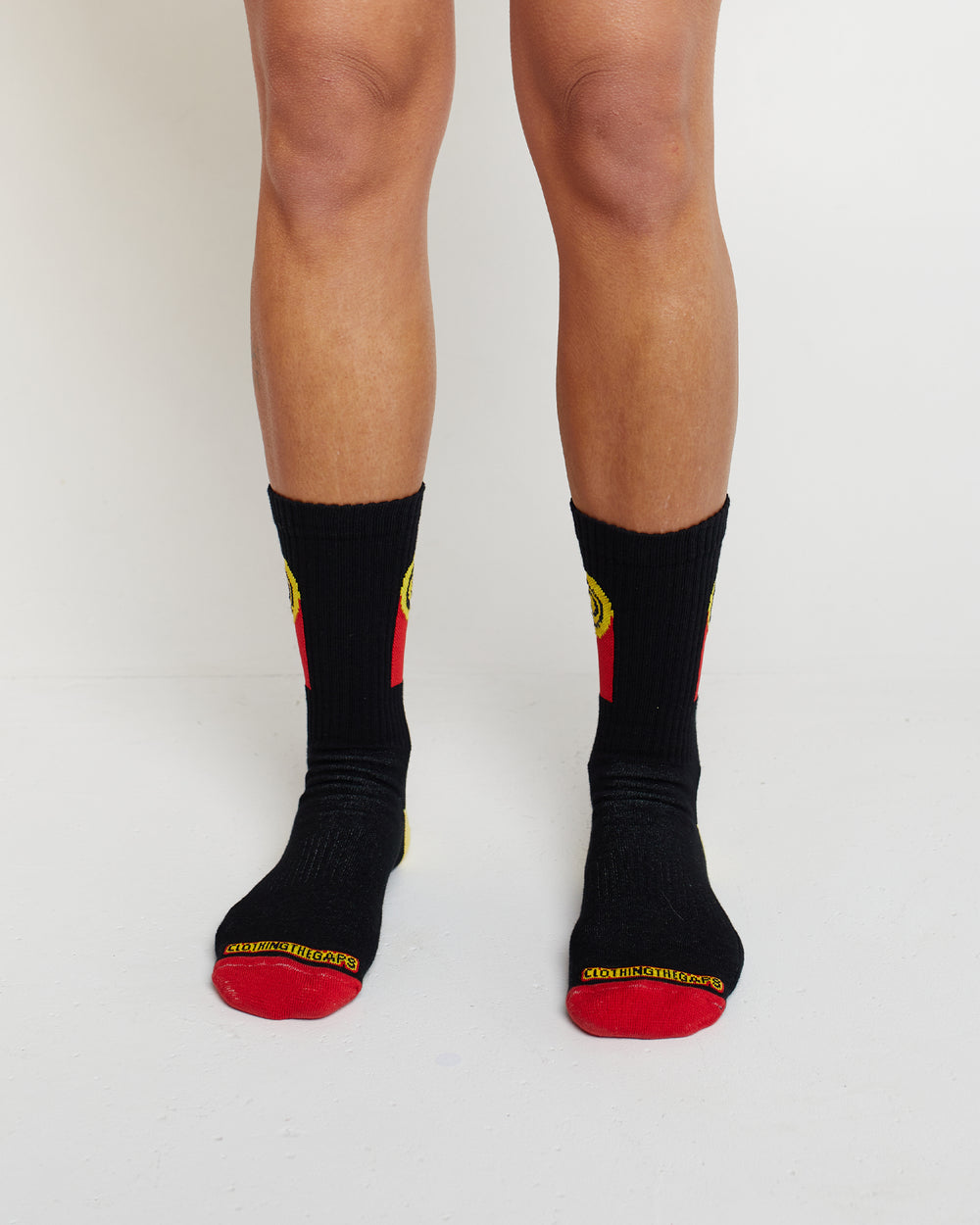 Clothing The Gaps. Flag Rights Socks. Long black socks with rectangle strips going down on both sides of socks representing the Clothing The Gaps logo and Aboriginal flag .With black at the top yellow circle in the middle with 2 black circular rings inside and red underneath the yellow. On both sides of each sock. Yellow on heel of socks. Red on toes of socks. Clothing The Gaps written above red section just going over toes.
