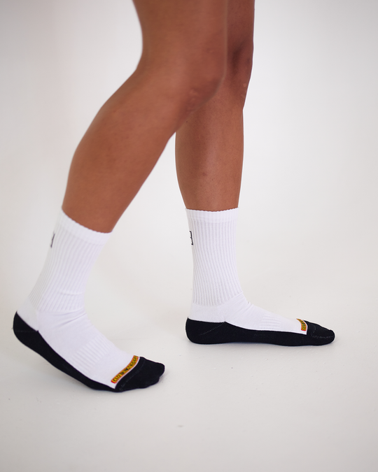 Clothing The Gaps. White Empty Flag Socks. Long white socks with black Aboriginal flag outline on back. Black on bottom of sock to hide dirt. Clothing The Gaps written above toe area.