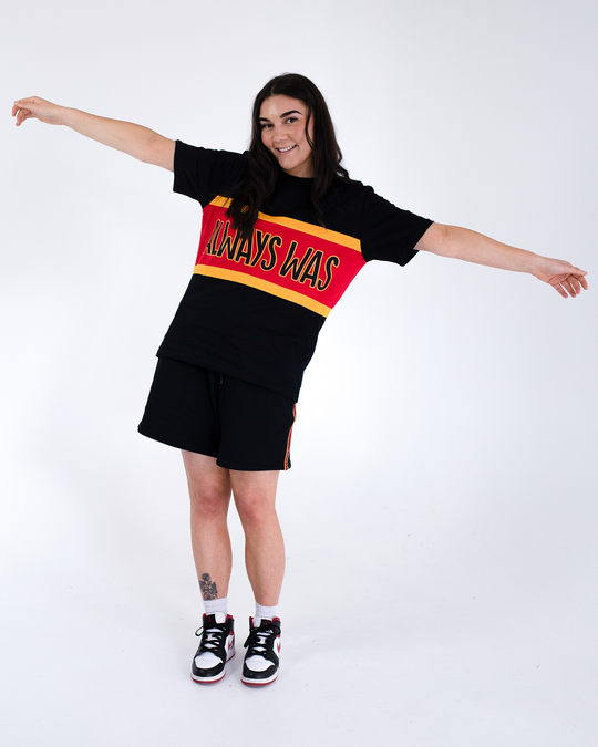 Clothing The Gaps. Power Rugby Tee. Red, black and yellow colorway. Black base tee with thick yellow top and bottom lines and red fill in mid section of jumper with big bold black text with a yellow outline in red section. Reading 'Always was' on front and on back in same text 'Always will be.'