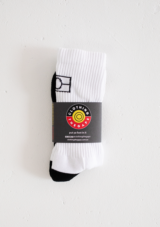 Clothing The Gaps. White Empty Flag Socks. Long white socks with black Aboriginal flag outline on back. Black on bottom of sock to hide dirt. Clothing The Gaps written above toe area.