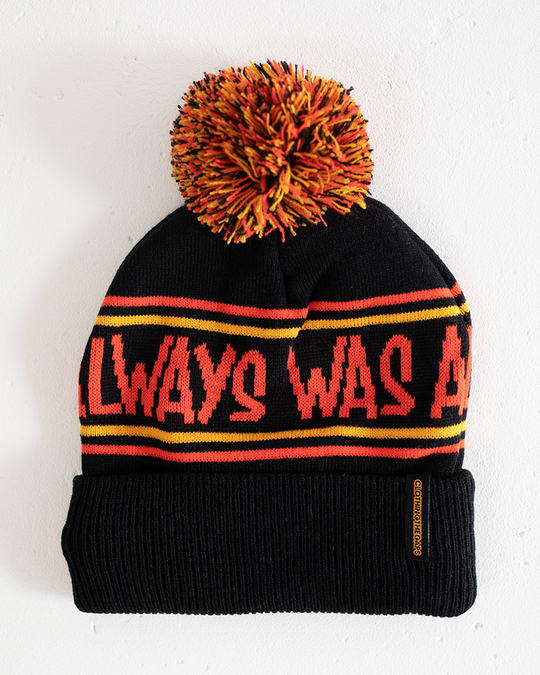 Clothing The Gaps. Power Beanie. Black base with two skinny red and yellow lines above and below bold capital red text 'Always was, Always will be.' Red, black and yellow pom on top of beanie. Embroidered clothing the gap.