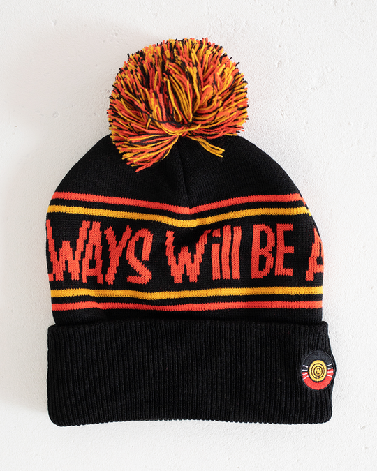 Clothing The Gaps. Power Beanie. Black base with two skinny red and yellow lines above and below bold capital red text 'Always was, Always will be.' Red, black and yellow pom on top of beanie. Embroidered clothing the gap.