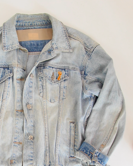 Clothing The gaps. Resistance Pin. Detailed brown resistance fist with red, black and yellow painted nails and aboriginal flag on wrist of fist. With gold outlines and backing.