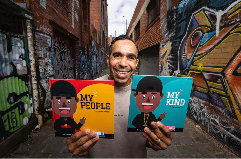 Clothing The Gaps. Eddie Betts’ Lil' Homies Books. Two books 'My Kind' and 'My People'. My Kind front cover features a cartoon version of Eddie with a blue background and the books title 'My Kind.' My People front cover features a cartoon version of Eddie with a red background and yellow sun with the books title 'My People'.