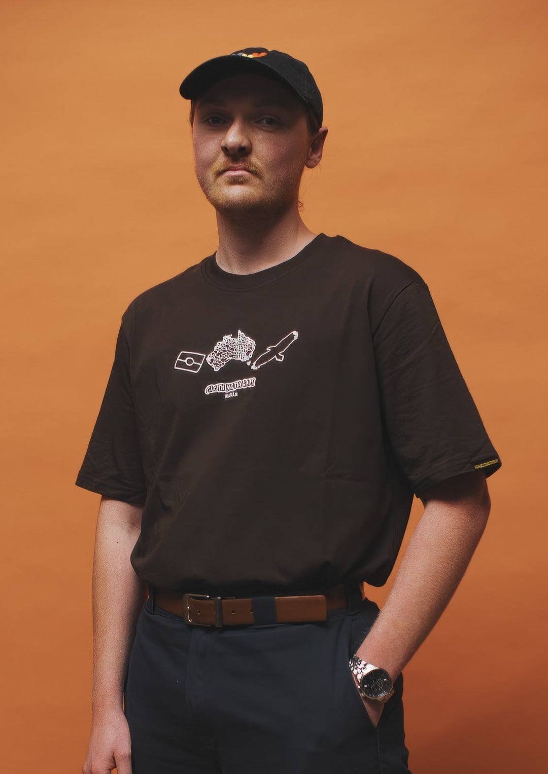 Clothing The Gaps. Icon Tee. Expresso dark brown tee featuring Aboriginal symbols of resistance and culture including a white outline of the Aboriginal flag, a white outlined decolonised map of “Australia” and a white outlined Bunjil, a well known wedge-tailed eagle - who is the spiritual creator and protector of the Kulin Nation in Victoria. These symbols are on the front of the tee across the chest.