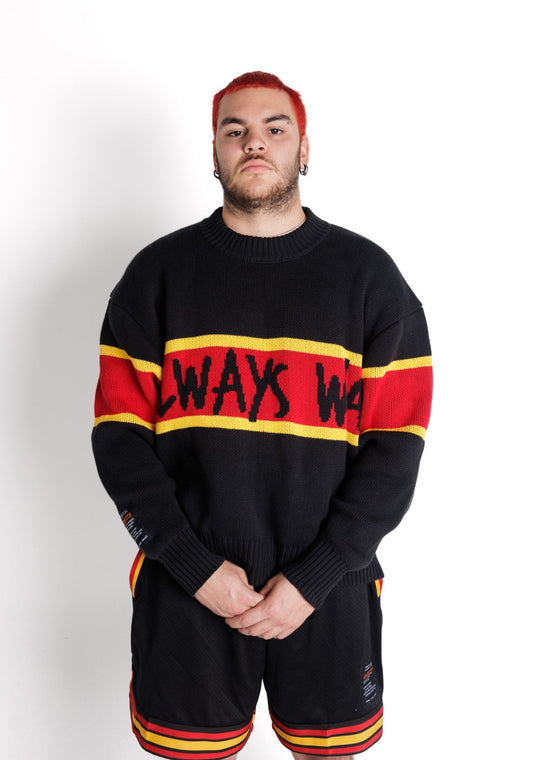Clothing The Gaps. Power Knit Jumper. Red, black and yellow colorway heavyweight 100% cotton oversized boxy fit. Black base with thick yellow top and bottom lines and red fill in mid section of jumper that flows into same pattern on sleeves. In red section on front of jumper in bold hand-written type capital text reads 'Always was' and on back in same text 'Always will be.' With black knitted cuffs and waistband.