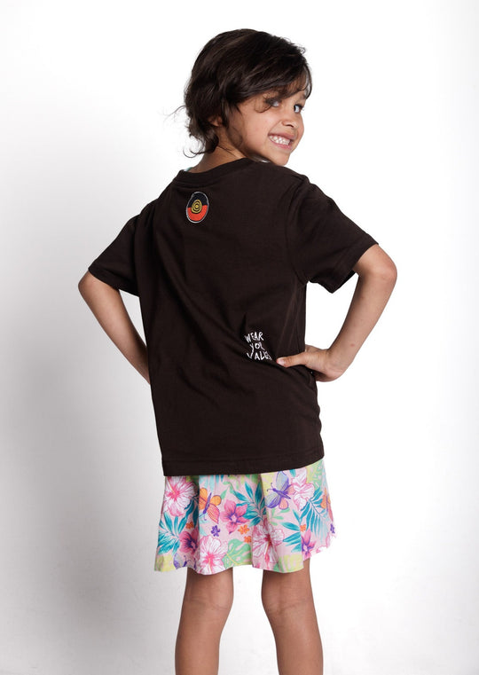 Clothing The Gaps. Kids Icon Tee. Expresso dark brown tee featuring Aboriginal symbols of resistance and culture including a white outline of the Aboriginal flag, a white outlined decolonised map of “Australia” and a white outlined Bunjil, a well known wedge-tailed eagle - who is the spiritual creator and protector of the Kulin Nation in Victoria. These symbols are on the front of the tee across the chest.