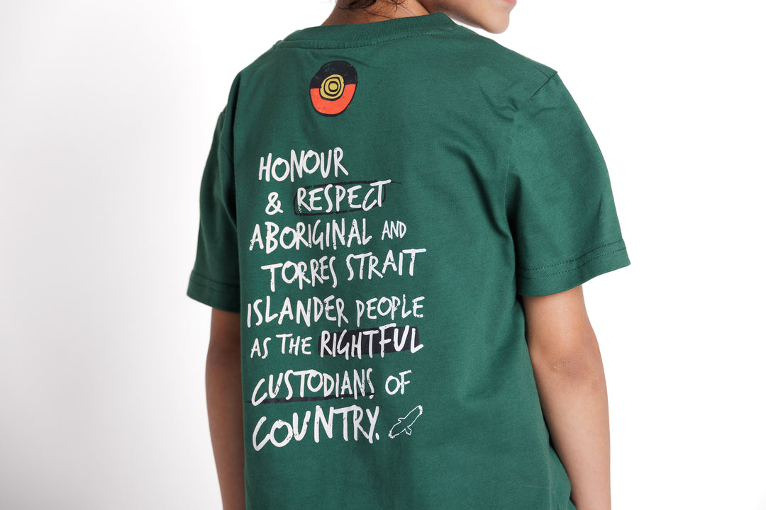 Clothing The Gaps. Kids Handwritten Honour Country Tee. Forrest green T-shirt with 'Honour Country' across chest in handwritten white text and coloured Aboriginal flag small underneath. On Back of tee white hand-writen style text 'Honour and respect Aboriginal and Torres Strait Islander people as the rightful custodians of country.' Circling 'respect' underlining 'custodians' and highlighting 'rightful' in a black colour. Outlined 'bunjil' eagle in bottom right corner.'        