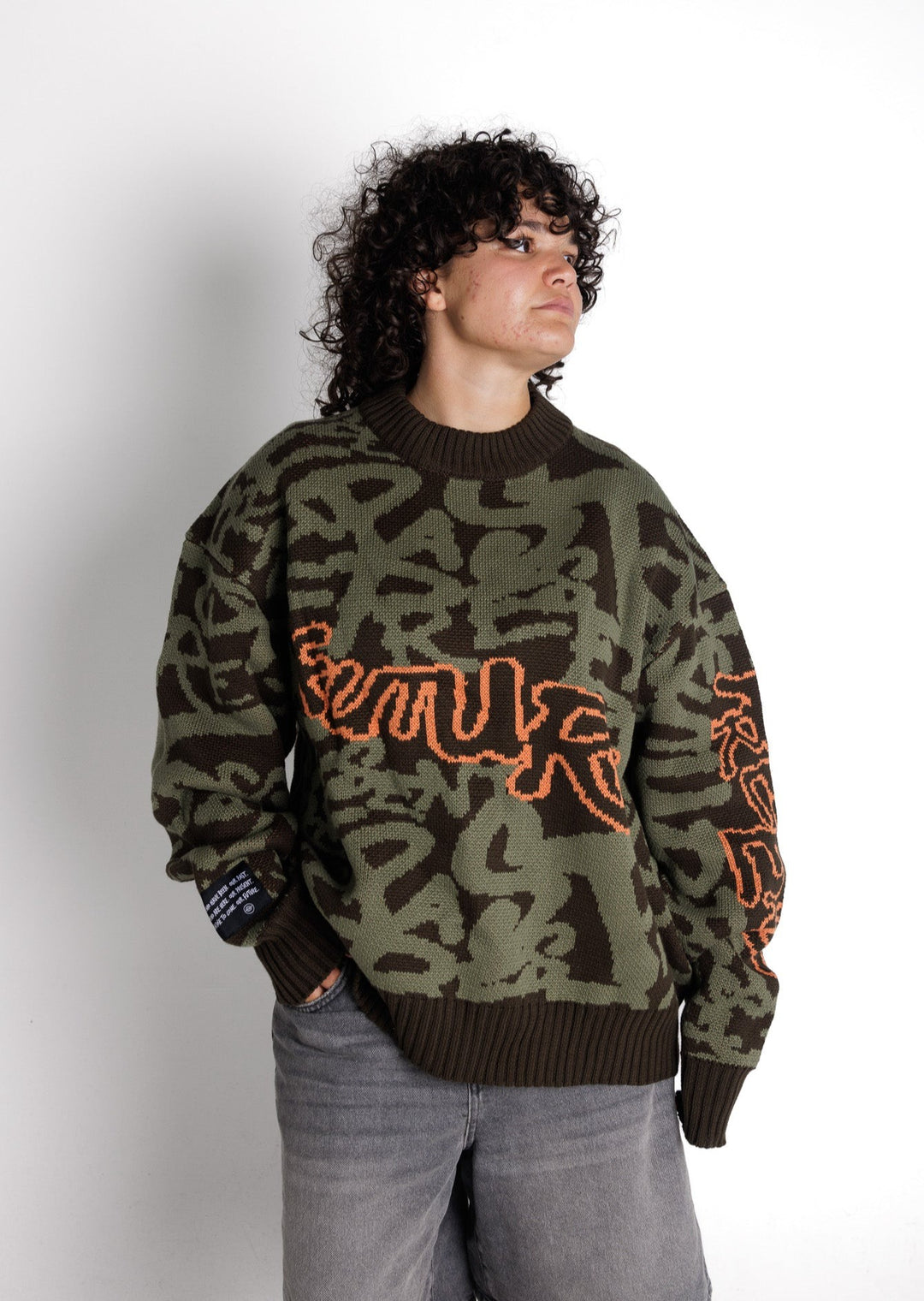 Clothing The Gaps. Past Present Future Knit Jumper. Khaki green colorway heavyweight 100% cotton oversized boxy fit. Has the words 'Past Present Future', in a kahki green graffiti background and 'future' on the front, 'past' on the back, and 'present' running down the arm in a orange outline. The background pattern seamlessly weaves the words past, present, and future. With khaki knitted cuffs and waistband.