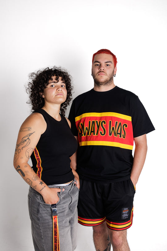 Clothing the Gaps. Black ribbed tank. With black 'always was always will be' text on a red background with a yellow trim. In a cotton tape strip going down under both arms.