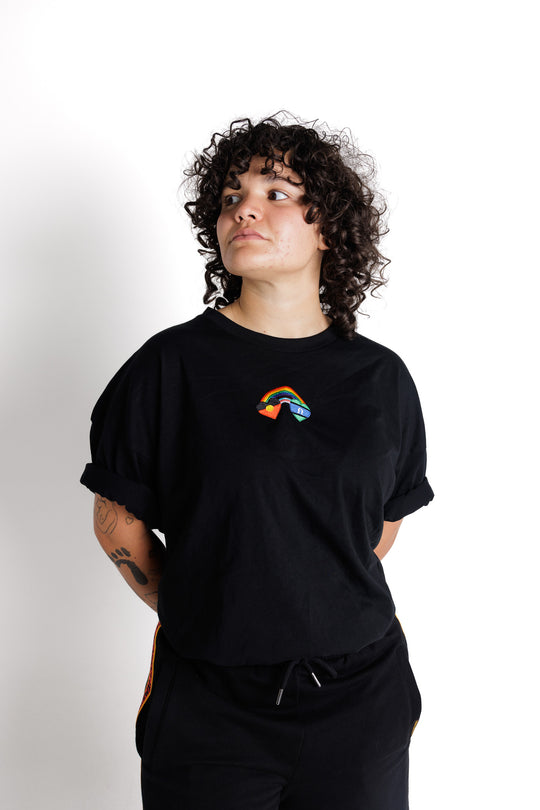 Clothing The Gaps. Blak Rainbow Luv Crop. All black boxy crop tee with  a heart featuring the Aboriginal flag at the start of a rainbow and at the end of the rainbow the Torres Strait Islander flag. The rainbow includes the colours from the progress pride flag. Show your pride or support for First Nations LGBTQIAS&B+ Community.