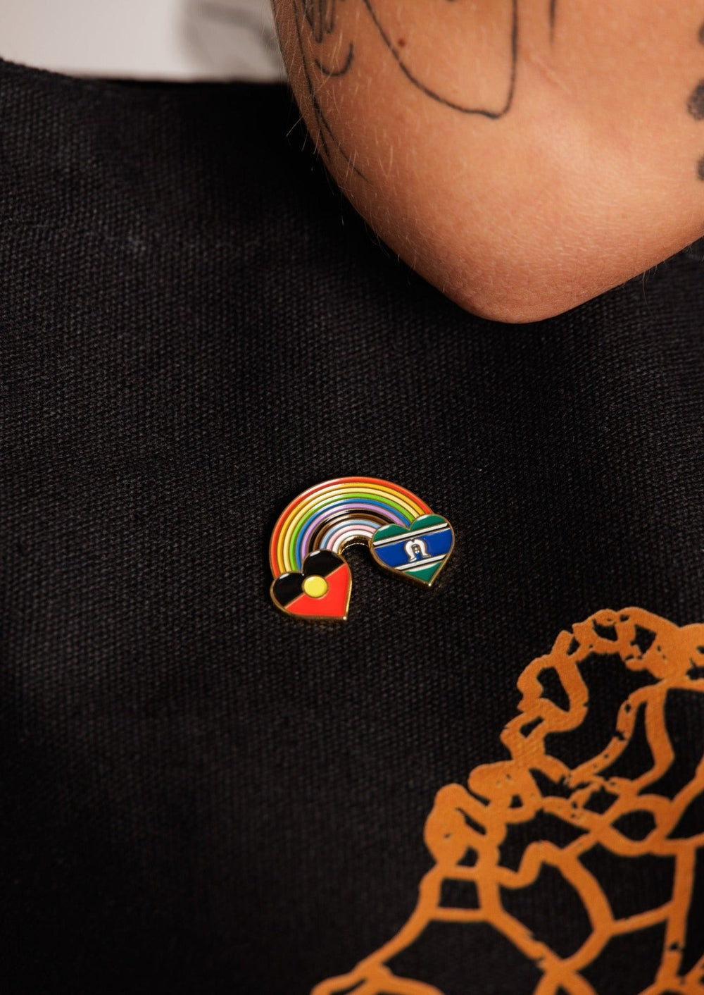 Clothing The Gaps. Rainbow Mob pin. Pin with Aboriginal flag in love heart shape at the start of a rainbow and at the end of the rainbow the Torres Strait Islander flag in love heart shape. The rainbow includes the colours from the progress pride flag. Show your pride or support for First Nations LGBTQIAS&B+ Community.