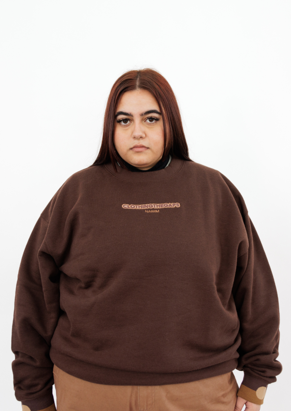 Clothing The Gaps. Chocolate Crew Jumper. Brown chocolate crew neck jumper. With tonal lighter brown 'Clothing the gaps' and the word 'Narrm' embroidered on the front of crewneck.' Wear your values' is also embroidered small on the back of the crew with the same light brown tonal colour. The wrist cuffs of the crew have a woven tonal brown aboriginal flag on them. 